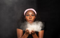 Black lash tech and makeup artist blowing setting powder in a photography studio during branding photoshoot in Indiana.