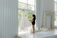 photo of a bride admiring her dress thats hanging up in her ceremony space