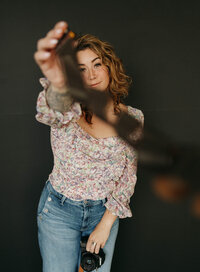 Jaime tossing a film strip playfully toward the camera while holding her camera in hand.