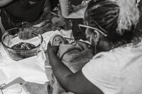 Birth photography in Tifton: midwife checks just-born baby wrapped in a blanket