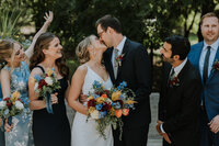 bride and groom kissing while bridal party cheers them on