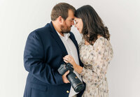Hunter and Katiera standing closely facing eachother with their foreheads touching holding their cameras
