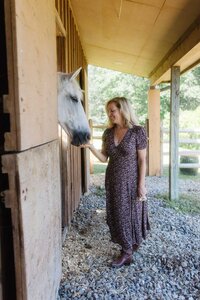 Leiko offering her hand to a white horse inside the barn at Peace Horse Collective, inviting trust and connection during an equine-assisted healing session in the Berkshires