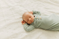 newborn baby on white bedding in a sage green onesie