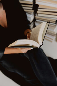 A woman reading a book, surrounded by stacks of literature, representing spiritual knowledge and awakening resources.
