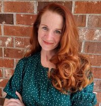 Jenn smiling in a green polka dot blouse, standing in front of a brick wall