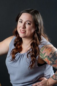 A professional portrait of a photographer with a camera tattoo  in front of a dark backdrop