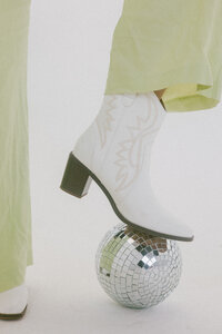 woman rests cowgirl boot on disco ball