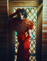 Woman wearing red dress from recycled fabric with light beams  by stained glass window