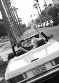 Bride and groom in retro car downtown Phoenix with bride waving bouquet in the air