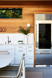 A modern outdoor kitchen in a new construction pool house with custom kitchen cabinets in Boston, light grey cabinetry, and a Sub-Zero glass door refrigerator.