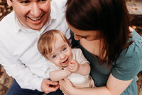 Mom and dad holding young son.  boy is looking up and smiling while clapping his hands.  photo taken by Philadelphia family photographer, Kristi