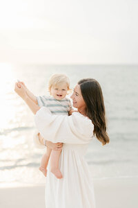 Mother with long brown hair and flowy dress walks the beach in Delaware with her daughter during a family photo session