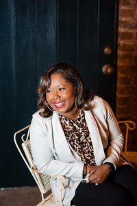 Woman sitting on chair wearing light blue blazer and smiling. Photo taken with off camera flash.