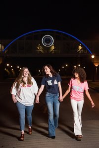 3 MTSU Greek life seniors walking on the Murfreesboro campus for senior pics at night with the walking bridge behind them