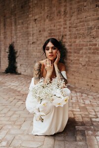 Bride squatting down in a moody pose with hands on face and floral bouquet in her lap