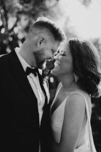 A close up of a bride and groom in black and white, touching noses, backlit by the afternoon sun