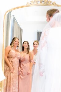 Bridesmaids look excitedly at the bride through the mirror at the Distillery.