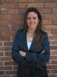 woman with long brown hair standing outside with her arms crossed smiling at the camera