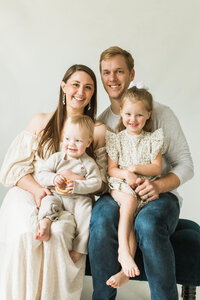 family of four sits in a studio to pose for family photo