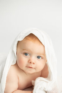 baby-boy-with-blues-under-white-blanket-smiling-for-sitter-session-in-columbus-ohio-amanda-estep-photography