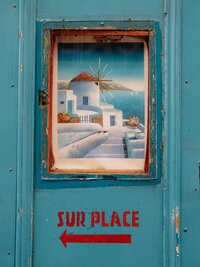 Close up of an artwork of Santorini agains a Blue wall with bright red writing in Greek