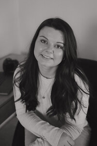 A black and white photo of Michaela with her arms crossed as she smiles up at the camera in her home office.