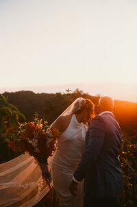 Film photo of a couple embracing at sunset in the mountains of Chiang Mai, Thailand during their elopement, with the bride holding a bold tropical bouquet — captured by a film wedding photographer.