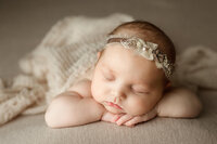 Newborn girl sweetly sleeping wearing a brown velvet headband.
