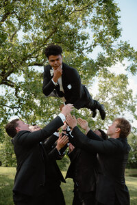 photo of the groomsmen throwing the groom in the air