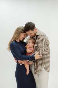 A pregnant mother rests her head on her husband's shoulder. She's holding a bouquet of flowers in one hand and her husband's hand in the other. He is holding their sonogram pictures.