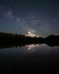 mountain and trees on a lake with night sky and stars