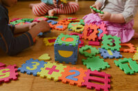 Children playing with a colorful numbered foam mat that forms a puzzle into math problems