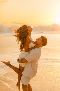 woman in her fiance's arms flinging her head back and smiling in makena beach