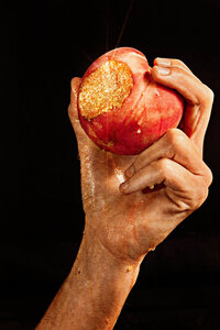 A striking and powerful image of a hand holding a peach with a bite taken out of it, set against a dark background. Photographed by Mica McCook, this composition emphasizes the natural beauty and rich texture of the fruit, creating a dramatic visual impact.