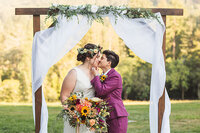 LBGTQ+ couple kissing under wedding arch