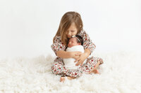 big sister holding newborn little sister so sweetly