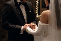A groom tenderly holds his bride’s hand as they exchange vows, captured in a luxury wedding photography style by TM Photo Co.