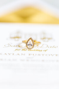 Gold wedding ring sits on top of luxury wedding invitation