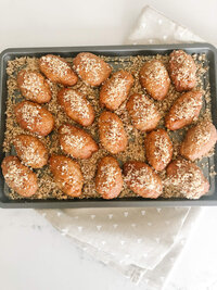 melomakarona (greek honey cookies)  on a black baking sheet topped with ground walnuts.