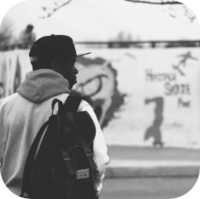 black and white photo of a man looking to the right wearing a baseball cap and bookbag over his shoulder