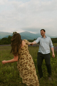 Couple holding hands and dancing through a field of lupins in the White Mountains of New Hampshire.