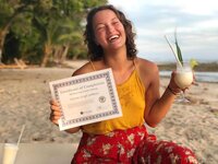 A happy graduate of Soma Yoga Institute's 200-hour certification program holds their certificate.