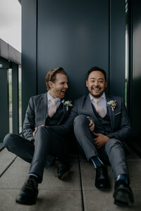 Male couple sitting on ground laughing during elopement portraits
