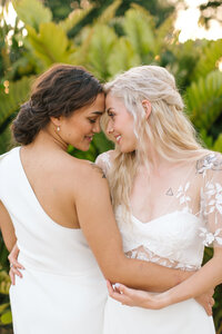 two brides hold each other at the waist and look into each. others eyes