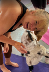 Woman in yoga attire petting a goat