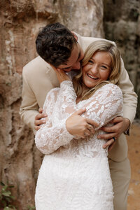 Candid moment as eloping couple exchanges kisses and smiles with red rock scenery behind them.