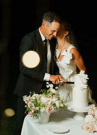 Adriana Montoya Photo, wedding photographer in Rexburg, Idaho. A bride kisses her groom on his cheek while he cuts their wedding cake at their wedding reception.