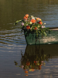 A canoe overflowing with colorful wedding florals floating on a lake at Camp Hale at a colorful Colorado wedding.