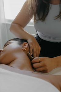 Femme allongée sur une table recevant un traitement de gua sha par une acupunctrice
